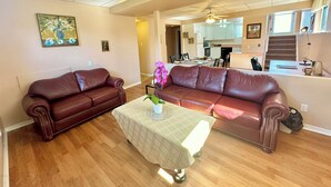 Ein großzügiger Wohnraum mit zwei braunen Ledersofas, einem Couchtisch mit Blumenvase und einem Essbereich im Hintergrund.