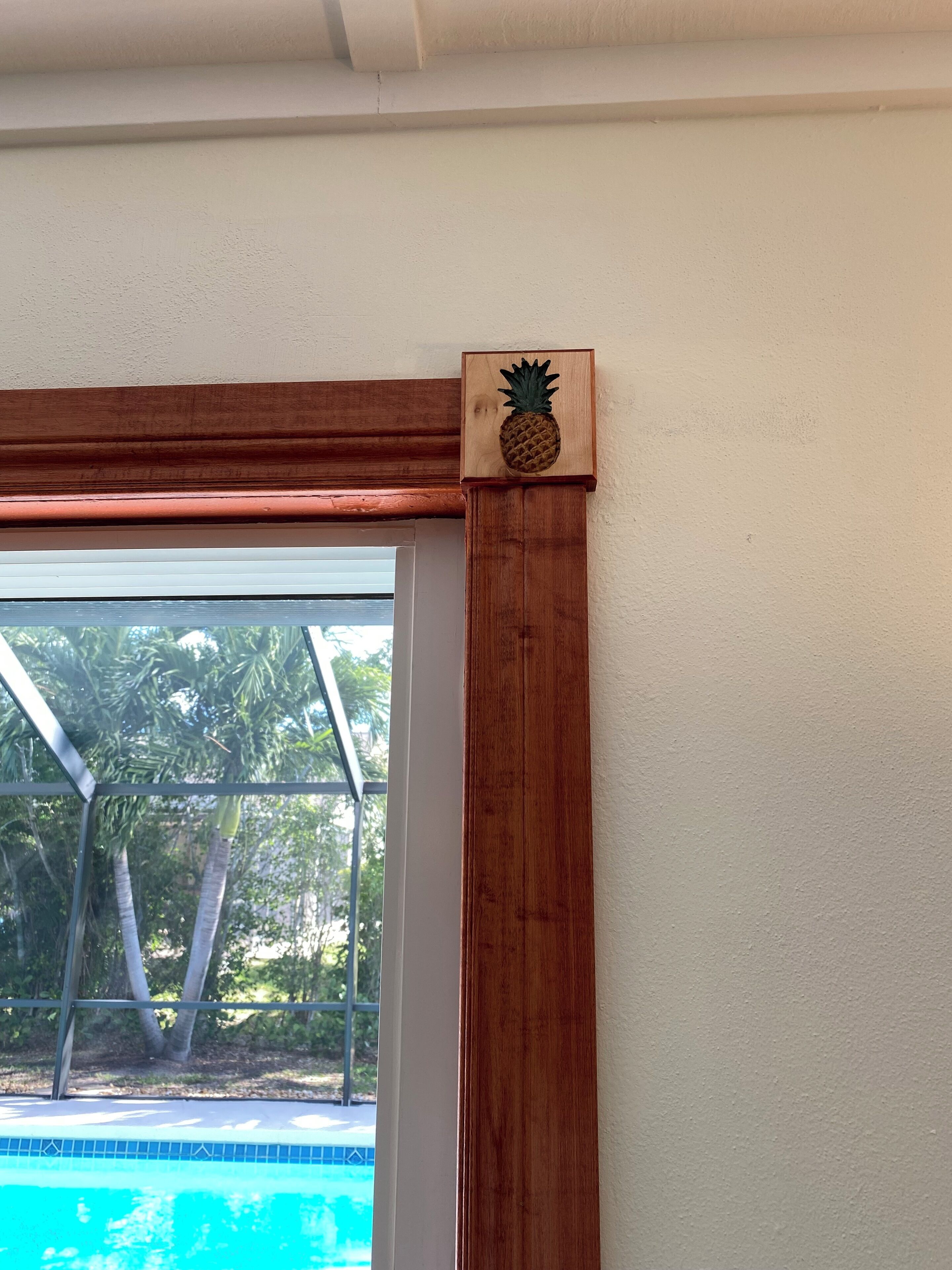 Moldura de madera con decoración de piña en la esquina de una ventana.
