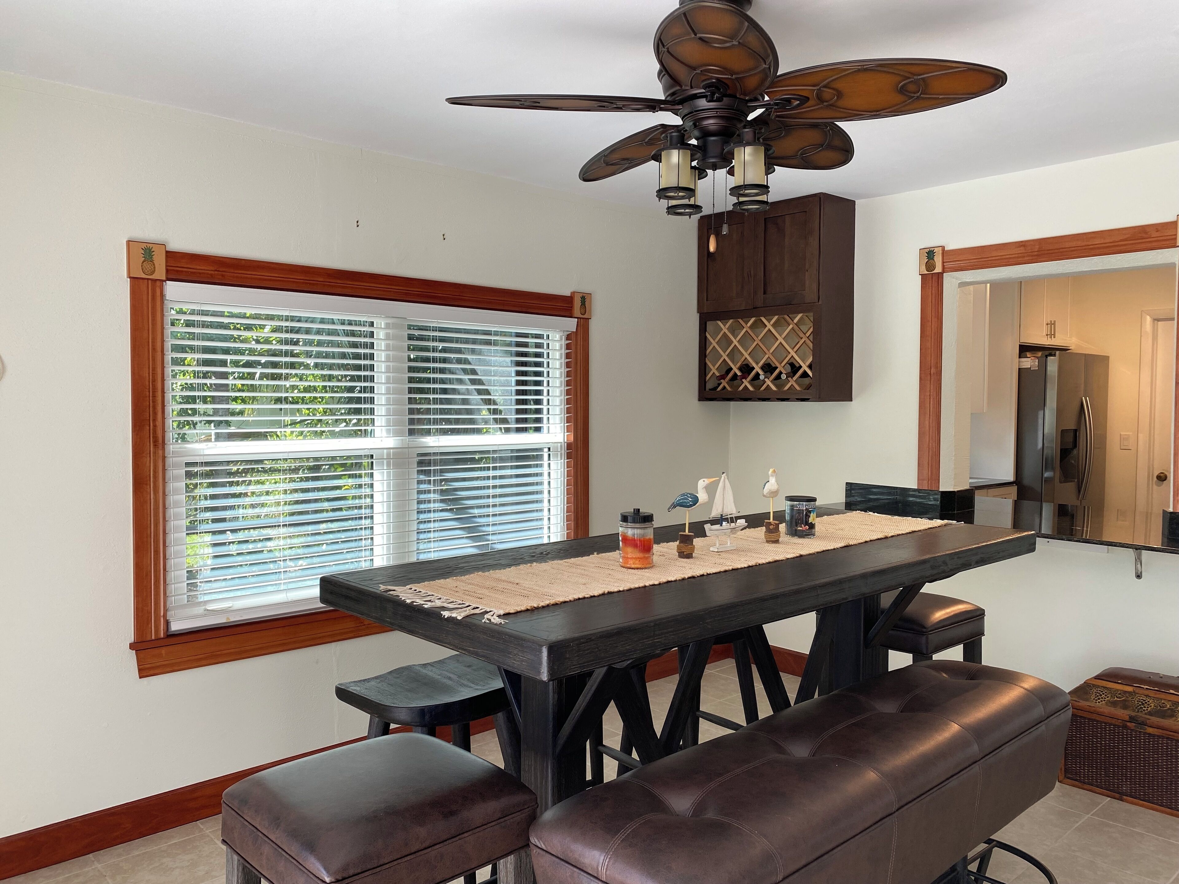 A dining area with a dark wooden table, two leather benches, a ceiling fan, and a window with blinds.