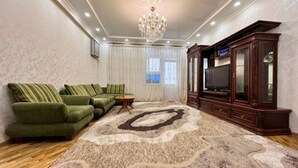 A living room with a sectional sofa, a large rug, a wooden cabinet, and a chandelier.