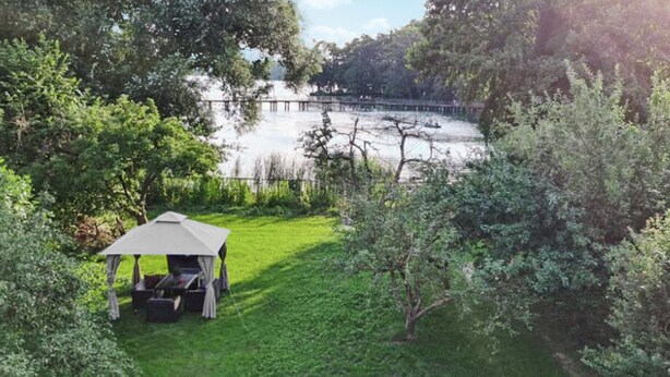 Ein Gazebo in einem üppigen Garten mit Blick auf einen See und einen hölzernen Steg.
