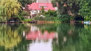 Ein ruhiger See mit einem Gebäude mit rotem Dach und üppigem Grün im Hintergrund.