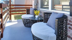Een balkon met rieten meubels, een glazen tafel en een vaas met gele bloemen.