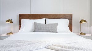 Een net opgemaakt bed met een houten hoofdbord, twee bedlampen en een gestreept kussen.