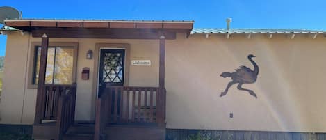 Een gebouw met een 'Welcome'-bord, een houten veranda en een muurschildering van een vogel.