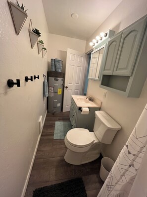 A compact bathroom with a toilet, sink, and vanity. There are decorative wall-mounted lights above the mirror, and a towel hanging on a hook. - The Ostrich House! Cozy, comfortable and private. (Eagar)