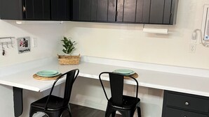 Una cocina moderna con armarios oscuros, encimera blanca, dos sillas negras y una pequeña planta.