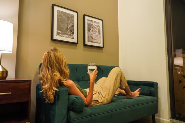 A person reclining on a green sofa in a room with a lamp and two framed pictures on the wall. - Central Park Jr. Suites (Quetzaltenango)