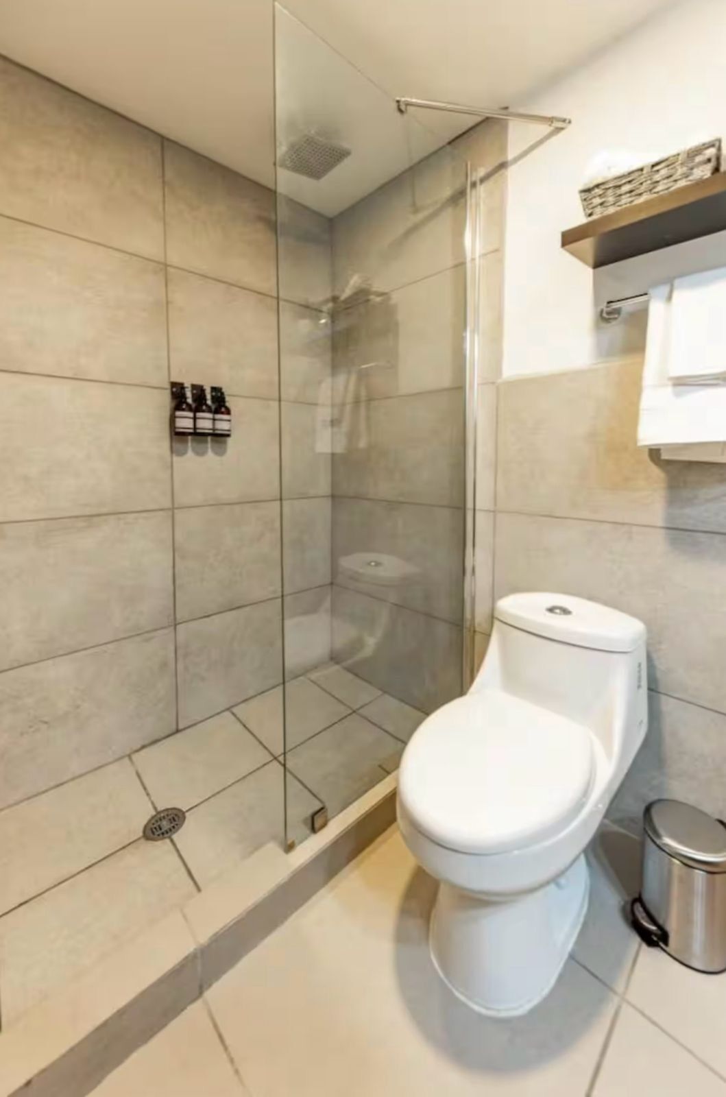 A modern bathroom with a glass-enclosed shower, a toilet, and a shelf with toiletries.