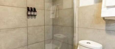 A modern bathroom with a glass-enclosed shower, a toilet, and a shelf with toiletries.