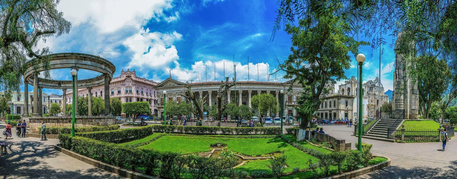 A public square with a central fountain, surrounding buildings, and a clear sky.