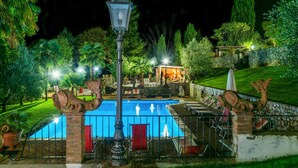Et poolområde om natten med en fontæne, en pergola og en statue.