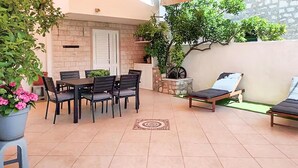 Une terrasse extérieure avec une table et des chaises, un fauteuil de relaxation et des plantes en pot.