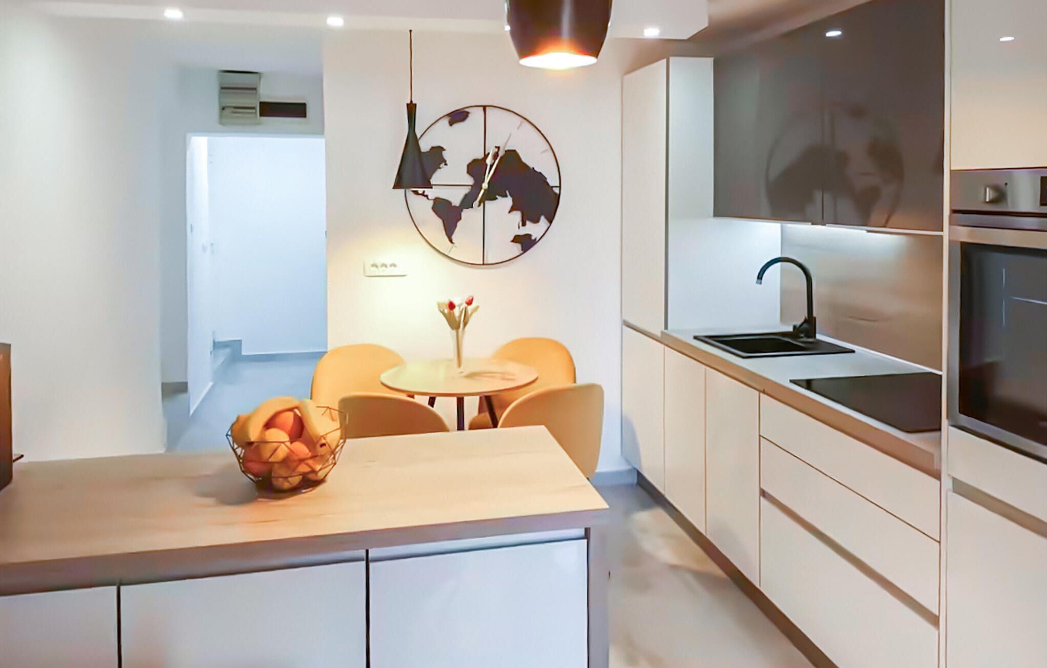 Une cuisine moderne dotée d’un îlot central, d’un coin repas avec une table ronde et des chaises, et d’une horloge murale.