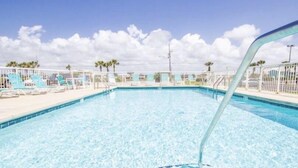 En swimmingpool med kristallklart blått vatten, omgiven av vita solstolar och ett vitt staket.