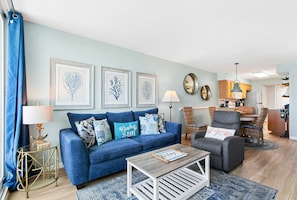 A living room with a blue sofa, a coffee table, and a dining area with chairs.