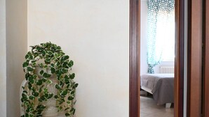 A room with a bed, a window with patterned curtains, and a plant in a white vase. - S347 – Sirolo, delightful two-room apartment with balcony (Sirolo)
