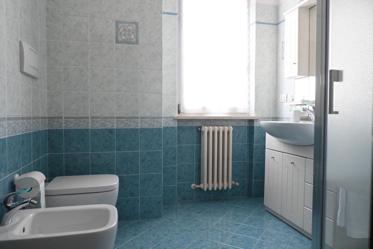 A bathroom with a toilet, bidet, sink, and a window with a view.