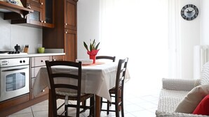 A kitchen with wooden cabinets, a dining table with chairs, a clock on the wall, and a window with curtains. - S347 – Sirolo, delightful two-room apartment with balcony (Sirolo)