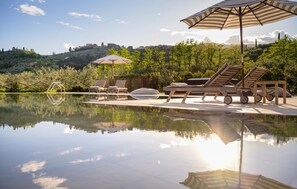 Un espace piscine paisible, agrémenté de chaises longues et de parasols, entouré d’une végétation luxuriante et offrant une vue dégagée sur les collines lointaines.