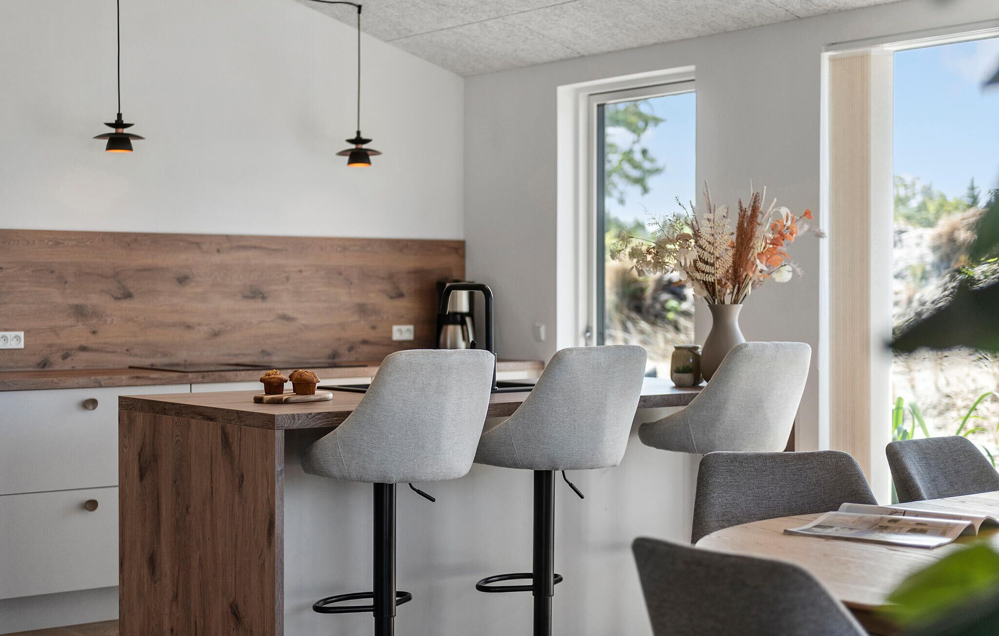 A modern kitchen with a wooden accent wall, bar stools, and a large window with a view of greenery.