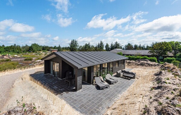 Una casa moderna con tetto spiovente, ampie finestre e un patio attrezzato con poltrone da relax.