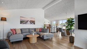 A modern living room with a grey sectional sofa, a round wooden coffee table, and a large potted plant. - Stunning home in Oksbøl with sauna (Oksbøl)