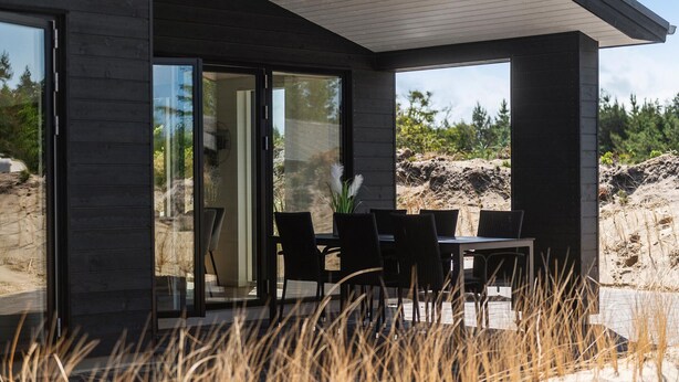 A modern outdoor dining area with a table and chairs, large glass doors, and a view of a natural landscape. - Stunning home in Oksbøl with sauna (Oksbøl)