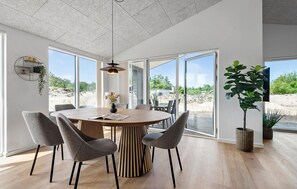 Un'area pranzo moderna con un tavolo rotondo in legno, sedie rivestite in grigio e una lampada a sospensione.