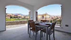 Un comedor con una mesa, sillas, pared de piedra y vistas a edificios y montañas.