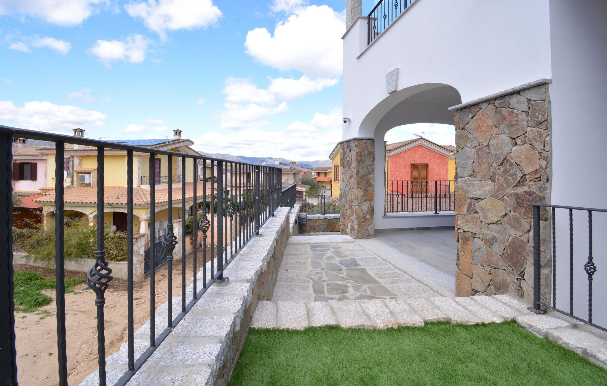 A residential area with a stone pathway leading to a building with a stone facade and an archway.