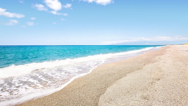 Una playa con orilla pedregosa y olas marinas tranquilas.