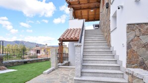 Una escalera de piedra que conduce a una pérgola de madera con techo de tejas, rodeada por un muro de piedra y otra escalera de piedra.
