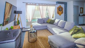 A modern living room with a grey sectional sofa, a small table with a lamp, a large mirror, and a dartboard on the wall. - Lovely home in Morières-lès-Avignon (Morières-lès-Avignon)