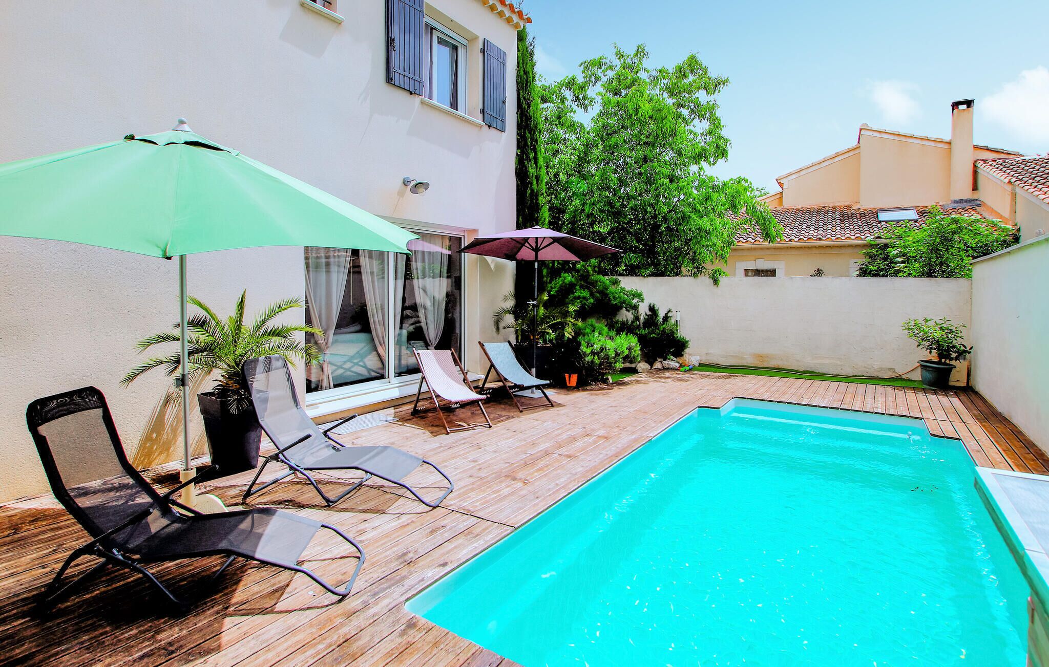 Ein Poolbereich mit Holzterrasse, zwei Liegestühlen und zwei Sonnenschirmen.