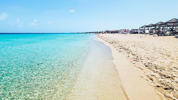 Une plage à l’eau turquoise et limpide, bordée d’un rivage sablonneux.