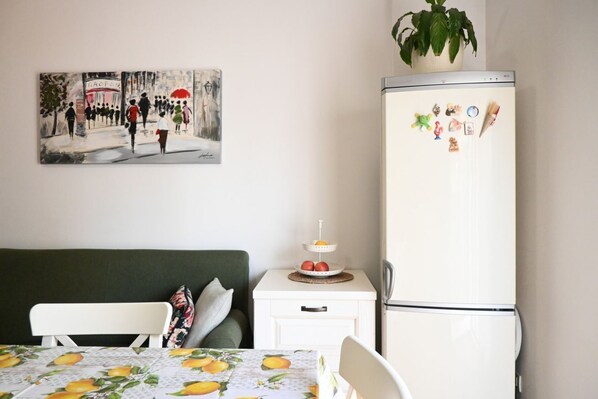 A bedroom with a bed, a nightstand with a plant, a refrigerator with magnets, and a painting on the wall.