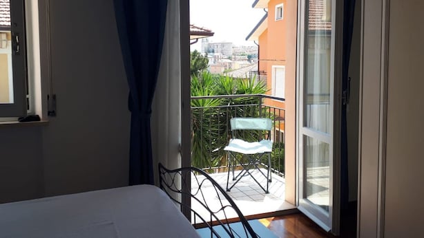 Una habitación con una cama, una ventana con cortinas y vistas a un balcón con una silla y plantas.