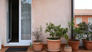 Entrada de un edificio con puerta corredera de vidrio, plantas en macetas y suelo de baldosas.