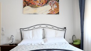 Una cama bien hecha con una colcha estampada, un cuadro en la pared y una mesita de noche con una lámpara.