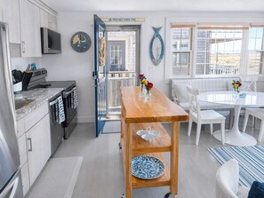 Una cocina moderna con una mesa y sillas de madera, un comedor con una mesa y sillas blancas, y vistas al exterior a través de una puerta.