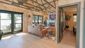 Una cabaña de madera con un espacio de sala que incluye un sofá, una mesa de centro y una chimenea. Un ventanal ofrece vistas al exterior.