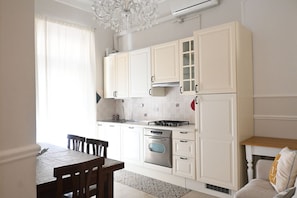 A kitchen with white cabinets, a gas stove, an oven, and a dining area with a table and chairs.