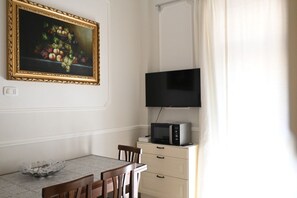 Un coin repas comprenant une table, des chaises, un bol, un tableau encadré, un four à micro-ondes et un téléviseur.