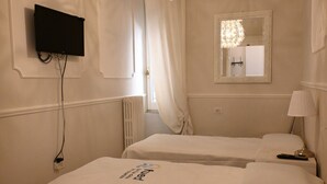 Ett hotellrum med två sängar, en tv som hänger på väggen, en spegel och en kristallkrona.