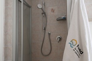 A shower with a handheld showerhead and a wall-mounted faucet, a towel hanging on a rack, and a door leading to another room. - P050 - Porto Recanati, elegant three-room apartment in the historic center (Porto Recanati)