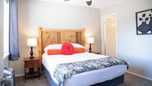Une chambre d’hôtel avec une tête de lit en bois, deux lampes de chevet, une couvre-lit à motifs floraux et un ventilateur de plafond.