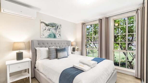 Un dormitorio moderno con una cama grande, una mesita de noche, una ventana con vistas a zonas verdes y un aire acondicionado instalado en la pared.