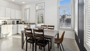 A modern kitchen with white cabinets, a dining table with chairs, and large windows with blinds.