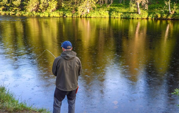 A person fishing by a calm lake surrounded by greenery.